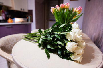 White roses flowers bouquet on wooden table against tulips.