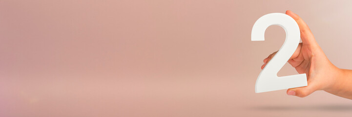 Number two in hand. Hand holding white number 2 on red background with copy space. Concept with number two. 2 percent, birthday 2 years old, couple, two, double