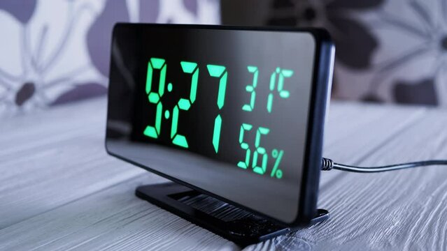 Digital Clock Showing Time on Green Display 9:27 AM, Temperature, Air Humidity. Modern mirror clock, alarm clock with a thermometer, hydrometer standing on a desk on white background. Time concept.