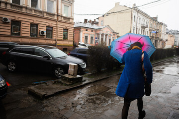 Woman with umbrella walking goes throw strong wind and rain in city street.