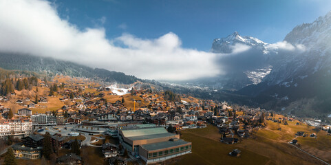 Obraz premium Aerial panorama of the Grindelwald, Switzerland village view near Swiss Alps mountains panorama landscape, wooden chalets on green fields and high peaks in background, Bernese Oberland, Europe.