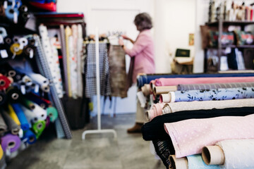 blurred woman in background. Rolls of fabrics in dressmaker's Atelier. Small business. fabrics shop