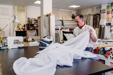 senior man working in atelier ironing curtains. Small business