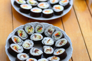 Plates with homemade sushi rolls on wooden table. Tuna and vegetable sushi, and vegetarian cream cheese and vegetable sushi. Selective focus.