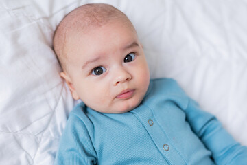 portrait of a cute baby in a blue bodysuit lying on his back in a white bed. View from above. The child is 4 months old. Space for text