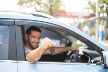 Close up at car key in young handsome man hand outta the windshield getting new car or rental a vehicle with happy and smiling. Male driving electricalc car on the road in his trip.