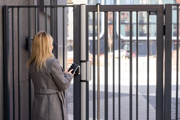 woman standing near the door and locking it with online application on her smartphone