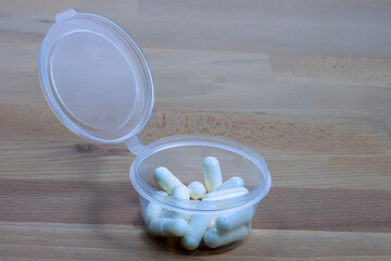 Packaging of medical pills in a plastic container on a wooden table. - 581901168