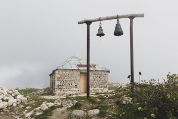 Old stone orthodox Saint Giorgi Church in Khvamli Mountain range in Georgia with simple wooden belfry with two bells, foggy weather.