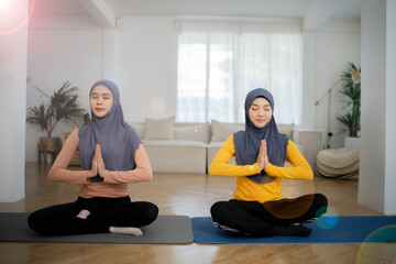 Two muslim girls do yoga at home, press hand at chest with intensingly on yoga mat with blur living room background.