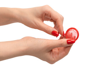 A red condom in a woman hand with red nails isolated on white background.