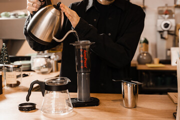Pouring hot water over roasted and ground coffee beans in aeropress. Process of aeropress alternative method brewing coffee. Barista is brewing aeropress coffee in cafe.