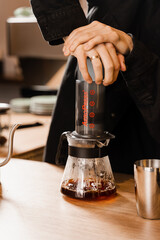 Fototapeta na wymiar Aeropress coffee. Barista is pushing aeropress for pouring coffee drops trought aeropress to pot. Alternative scandinavian coffee brewing method.
