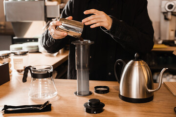 Barista pour ground coffee over aeropress before pouring water from drip kettle. Process of brewing aeropress coffee in cafe.