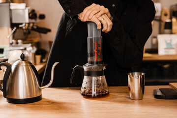 Aeropress coffee. Barista is pushing aeropress for pouring coffee drops trought aeropress to pot. Alternative scandinavian coffee brewing method. - obrazy, fototapety, plakaty