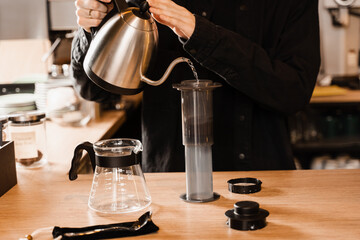 Pouring hot water over roasted and ground coffee beans in aeropress. Process of aeropress alternative method brewing coffee. Barista is brewing aeropress coffee in cafe.