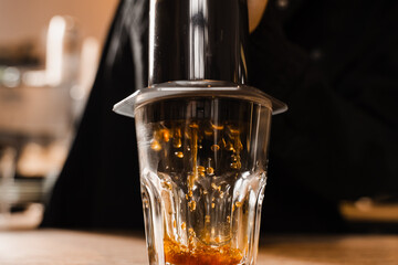 Falling coffee drops in cup close-up. Aeropress coffee. Process of pouring coffee in cup. Barista is pushing aeropress for pouring coffee drops.