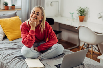 A cute college student with glasses is studying on the bed