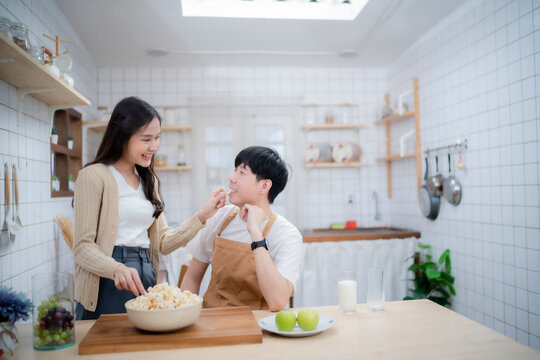 Couple of love enjoy with firting by sharing food together, girl feed boyfriend with piece of popcorn at kitchen.