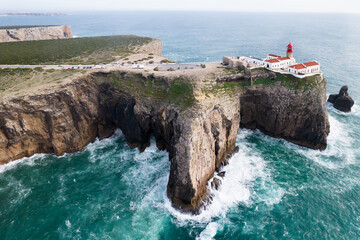 The lighthouse on high cliffs and strong waves hitting the rock at Cape St. Vincent. Continental...