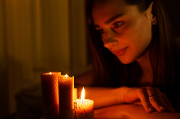 A woman holds a burning candle in her palms on a dark black background