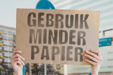The phrase " Use less paper! " on a banner in men's hand with blurred background. Human impact on the environment. Environmental degradation. Nature. Forest. Trees. Modern technology