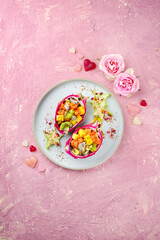 Traditionelle Valentinstag Fruchtsalat mit exotischen Fruchtstücken serviert in Drachenfrucht Schalen und dekoriert mit Sternfrucht auf einem Nordic Design Teller als Draufsicht mit Textfreiraum 