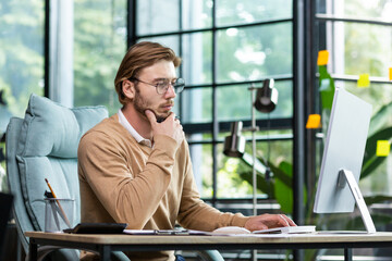 A young male businessman is concentrating on working from a home office at a computer.