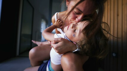 Mother kissing child son. Candid authentic real life mom kisses little boy in cheek embrace