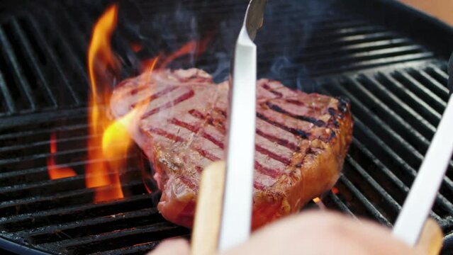 Barbecue wagyu porterhouse beef steak grilled as close-up on a charcoal grill with fire and smoke &ndash; video and audio 