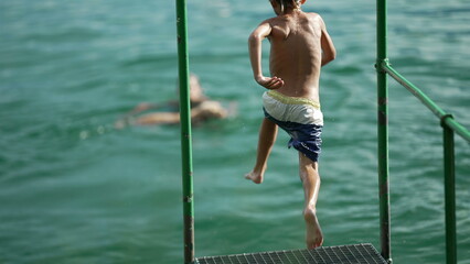 Fototapeta premium Kid plunging into lake water. Child having fun running by dock and jumps in river in super slow motion
