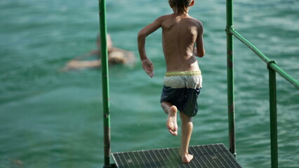 Kid plunging into lake water. Child having fun running by dock and jumps in river in super slow motion