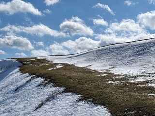 Sky clouds over hill with melting snow and dry grass.