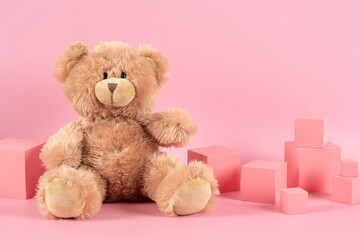 Baby kid toys background. Blue empty rectangle podium platform stand, teddy bear and pink wooden toy blocks on pastel pink background. Front view