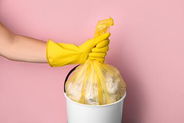Woman taking garbage bag out of rubbish bin on pink background