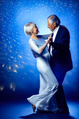 Fototapeta premium Elderly senior couple, man in dark suit and lady in elegant dress dancing on blue background with copy space, generative ai