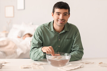Young man dipping mustard plaster into bowl of water in bedroom