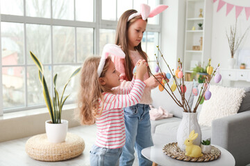 Little girls decorating tree branches with Easter eggs at home