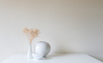 Dried baby's breath flowers in white vase on table against beige wall (selective focus)