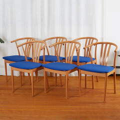 Set of Mid-century modern minimalist wooden chairs with a blue seats. 1960s wishbone-style chairs. Front view in front of long white curtain. 