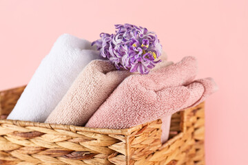 Wicker basket with folded soft towels and hyacinth flower on pink background