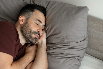 Man napping holding hands behind head sleeping on side, lying on soft pillow in cozy bedroom, copy...