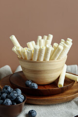 Bowls with delicious wafer rolls and blueberries on brown background