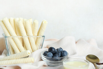 Fototapeta na wymiar Bowls with delicious wafer rolls and blueberries on white grunge background