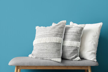 Stylish decorative pillows on bench near blue wall