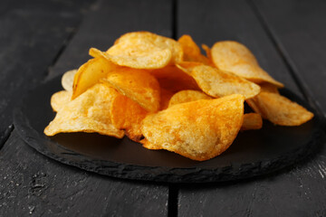 Slate board with delicious potato chips on black wooden background