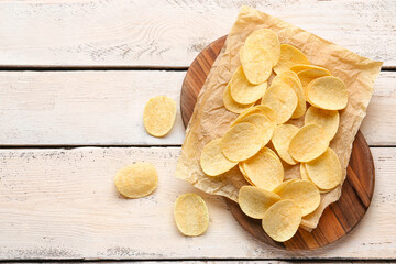 Board with delicious potato chips on white wooden background