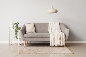 Interior of light living room with grey couch, table and lamp