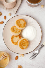 Plate with tasty cottage cheese pancakes with sour cream on light background