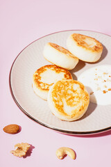Plate with tasty cottage cheese pancakes and sour cream on pink background, closeup